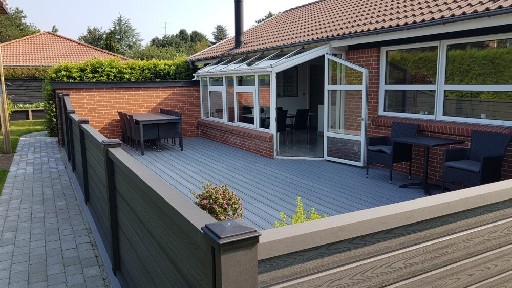 Terrassehegn ved rødstenshus. Gråsort komposithegn med træstruktur og betongrå komposit terrasse.